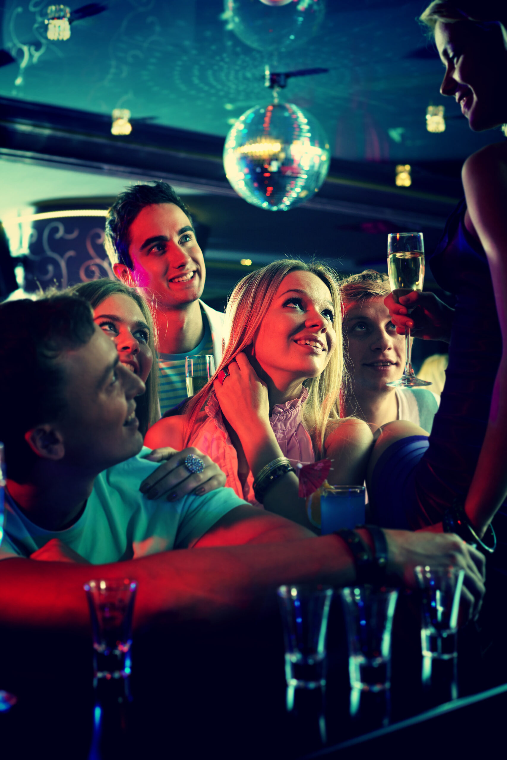 Portrait of cheerful girls and guys with cocktails looking at their friend in the bar